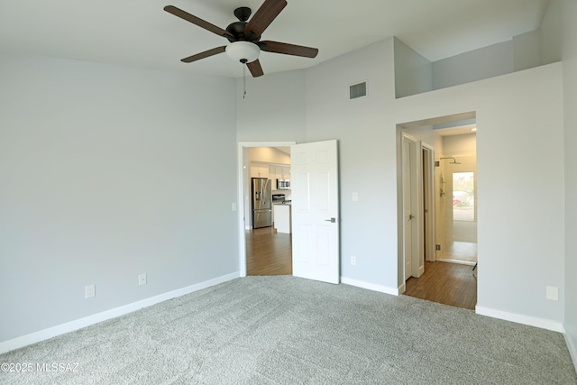 unfurnished bedroom with ensuite bath, ceiling fan, a high ceiling, dark colored carpet, and stainless steel fridge