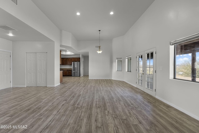 unfurnished living room featuring french doors, a towering ceiling, and hardwood / wood-style flooring