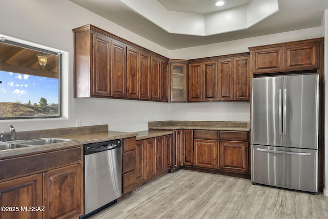 kitchen featuring dark countertops, glass insert cabinets, appliances with stainless steel finishes, light wood-style floors, and a raised ceiling
