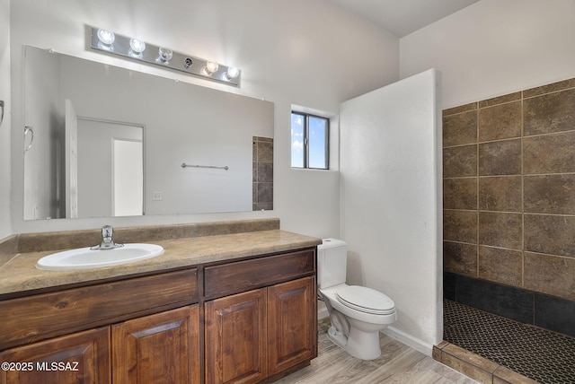 bathroom with toilet, wood finished floors, vanity, and a tile shower