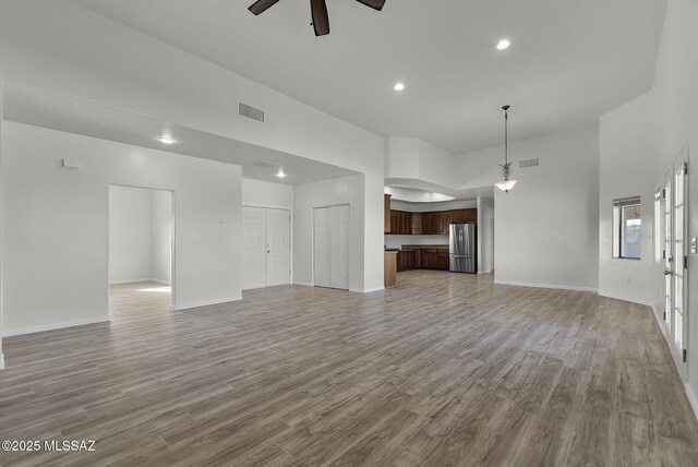 unfurnished living room featuring ceiling fan, a high ceiling, and light hardwood / wood-style flooring