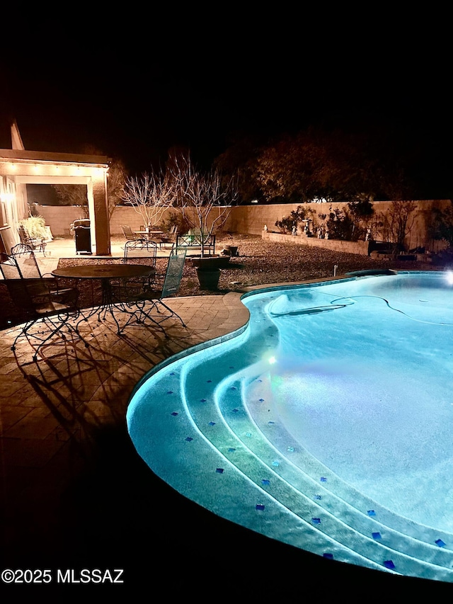 pool at night featuring a patio, fence, and a fenced in pool