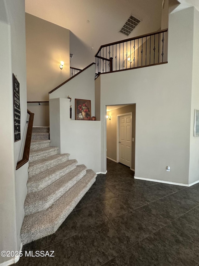 stairway featuring tile patterned floors, a towering ceiling, visible vents, and baseboards