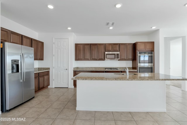 kitchen with sink, light stone counters, light tile patterned floors, a kitchen island with sink, and appliances with stainless steel finishes