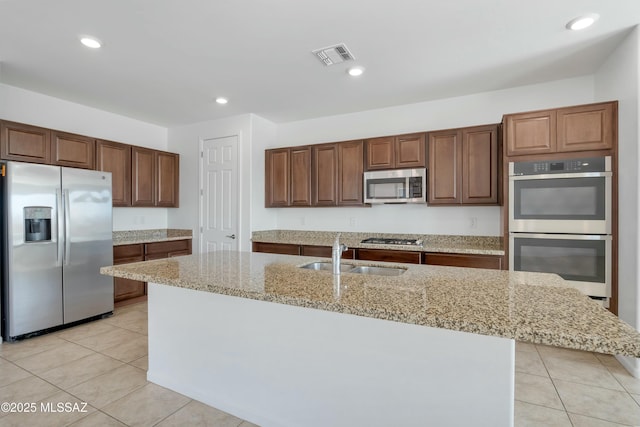 kitchen with stainless steel appliances, a center island with sink, sink, and light stone counters