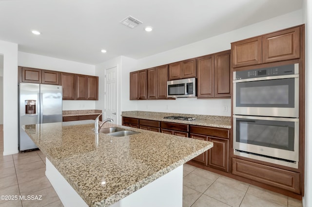 kitchen featuring sink, light stone countertops, a kitchen island with sink, and appliances with stainless steel finishes