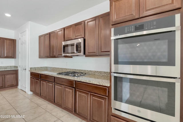 kitchen featuring stainless steel appliances, light tile patterned flooring, and light stone countertops