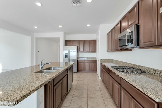 kitchen featuring light stone countertops, stainless steel appliances, an island with sink, light tile patterned flooring, and sink