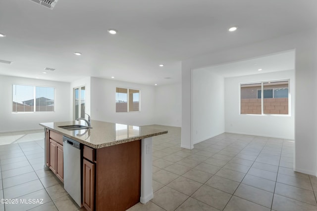 kitchen with sink, light stone counters, light tile patterned floors, stainless steel dishwasher, and a kitchen island with sink