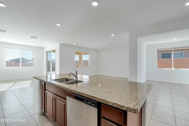 kitchen featuring sink, dishwasher, light stone counters, light tile patterned floors, and a kitchen island with sink