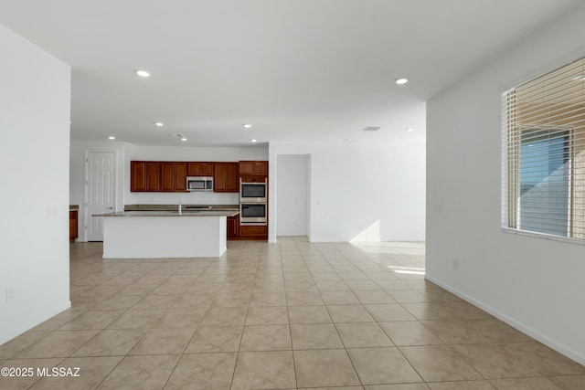 kitchen featuring light stone countertops, stainless steel appliances, a center island with sink, and light tile patterned floors