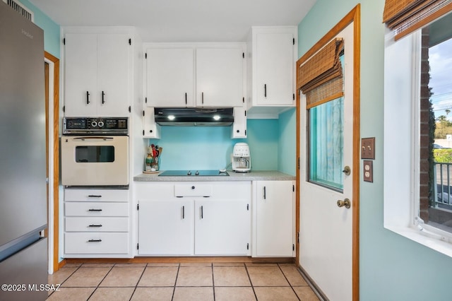 kitchen with white cabinetry, white oven, stainless steel fridge, black electric cooktop, and light tile patterned flooring