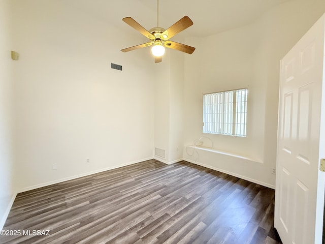 unfurnished room with ceiling fan, a towering ceiling, and dark wood-type flooring