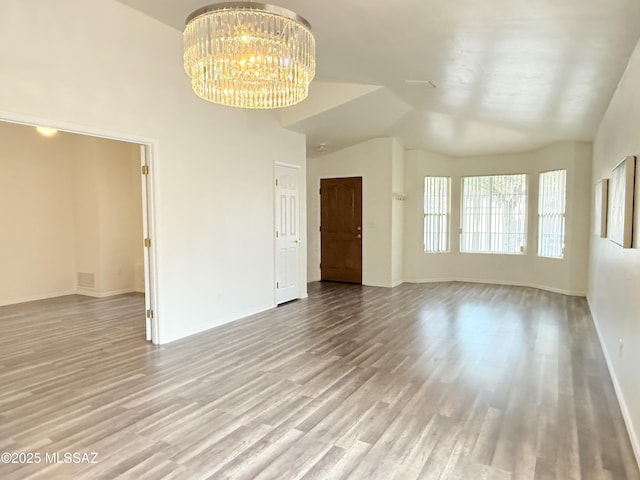 empty room with lofted ceiling, light wood-type flooring, and a notable chandelier