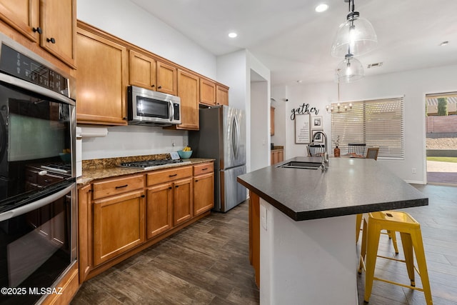 kitchen with pendant lighting, appliances with stainless steel finishes, an island with sink, sink, and a breakfast bar