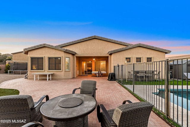 back house at dusk with a fenced in pool, a patio area, and a trampoline