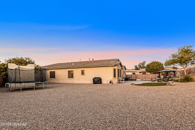 back house at dusk with a gazebo, a patio, and a trampoline