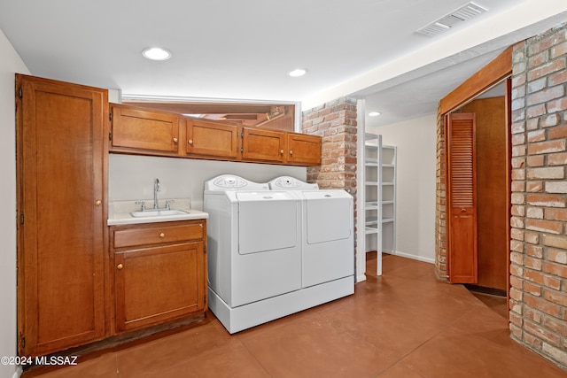 laundry room with light tile patterned floors, washer and clothes dryer, brick wall, cabinets, and sink