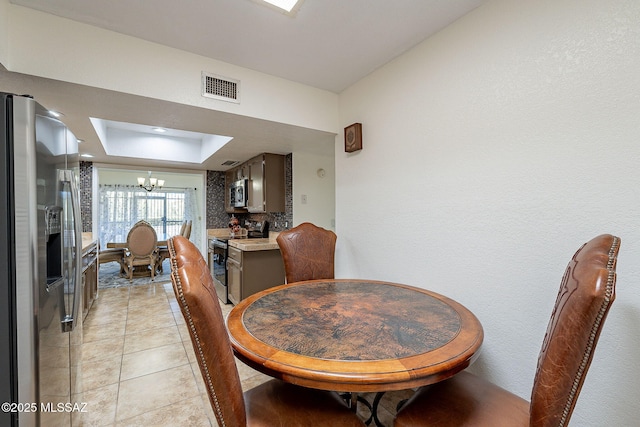 dining space with a raised ceiling, an inviting chandelier, and light tile patterned flooring