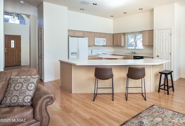 kitchen featuring white appliances, a towering ceiling, a breakfast bar, and a center island