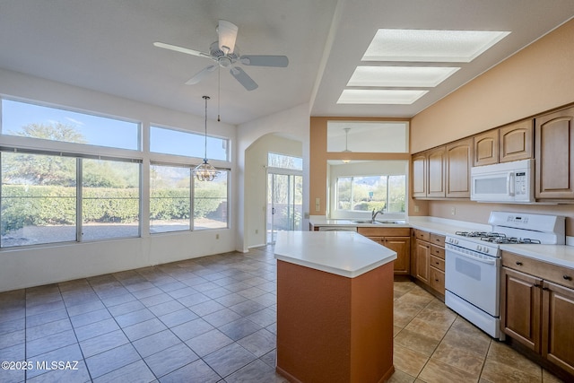 kitchen featuring tile patterned floors, pendant lighting, a kitchen island, white appliances, and ceiling fan with notable chandelier