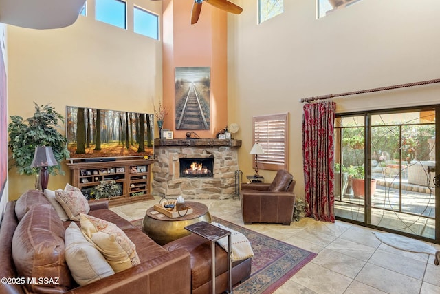 tiled living room with ceiling fan, a healthy amount of sunlight, a stone fireplace, and a towering ceiling