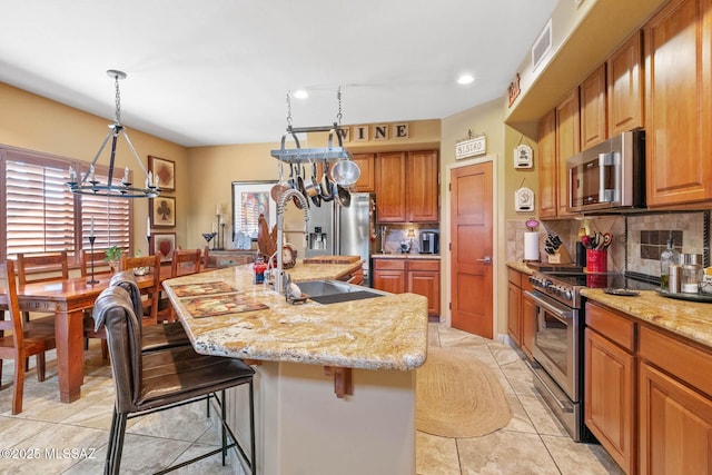 kitchen with light stone countertops, sink, stainless steel appliances, a kitchen bar, and a center island with sink