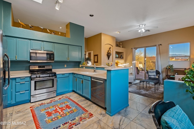 kitchen with appliances with stainless steel finishes, blue cabinets, sink, ceiling fan, and kitchen peninsula