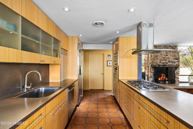 kitchen featuring sink, dark tile patterned floors, a fireplace, island exhaust hood, and stainless steel appliances