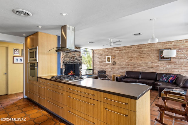 kitchen with ceiling fan, stainless steel appliances, brick wall, island range hood, and a fireplace