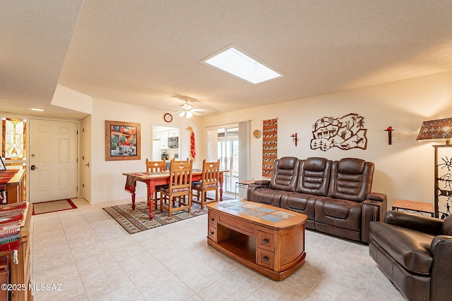 living room with ceiling fan, a skylight, and a textured ceiling