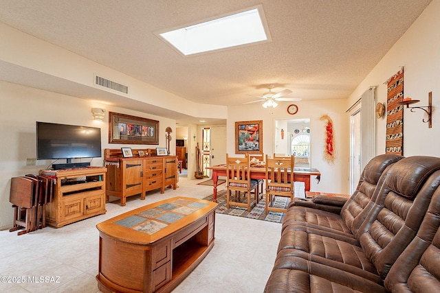 living room featuring ceiling fan, a textured ceiling, and a skylight