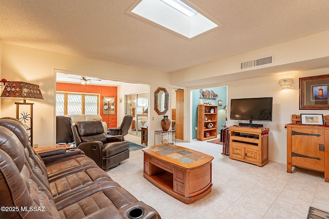 living room featuring ceiling fan, a skylight, and a textured ceiling