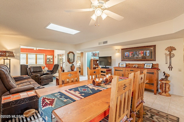 tiled dining room featuring ceiling fan, a skylight, and a textured ceiling