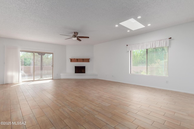 unfurnished living room featuring a textured ceiling, a skylight, light hardwood / wood-style flooring, and ceiling fan