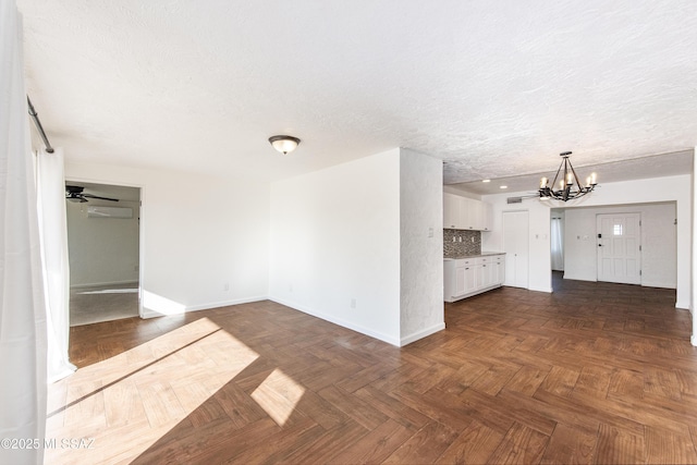 unfurnished living room featuring dark parquet flooring, ceiling fan with notable chandelier, and a textured ceiling