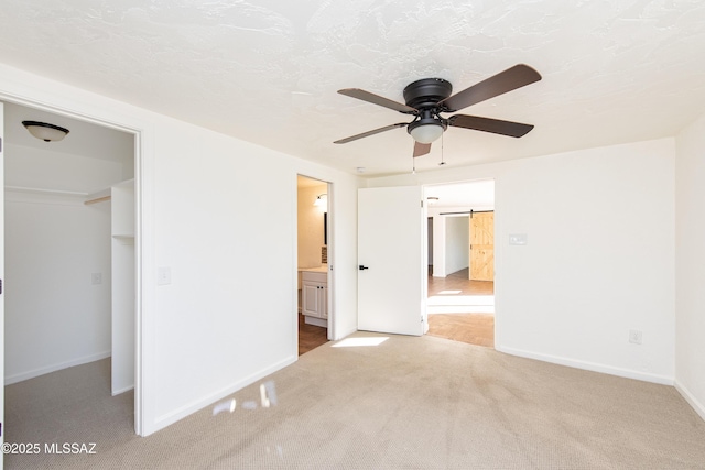 unfurnished bedroom featuring connected bathroom, carpet floors, a barn door, a walk in closet, and a closet