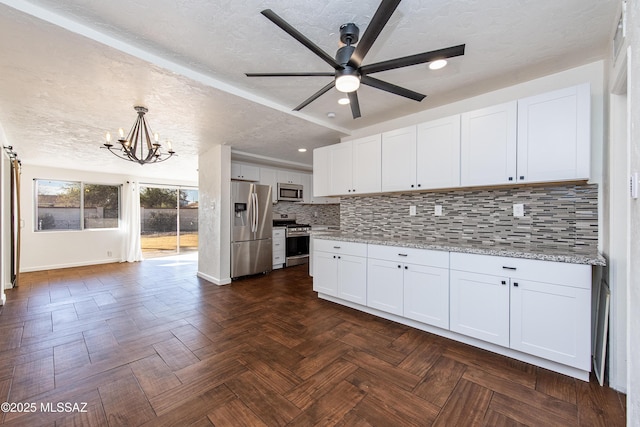 kitchen featuring white cabinetry, hanging light fixtures, stainless steel appliances, light stone counters, and ceiling fan with notable chandelier