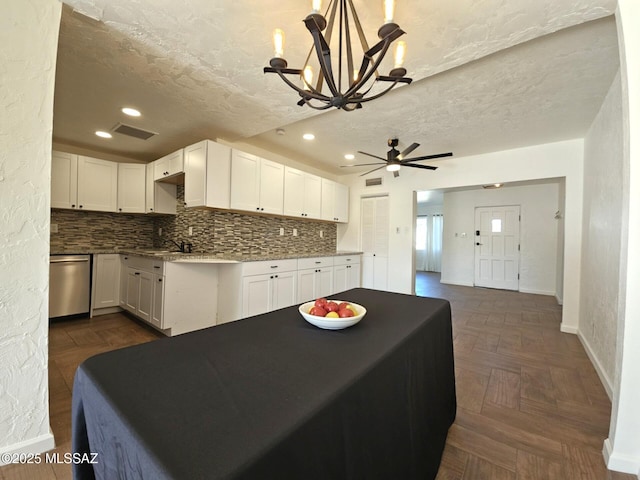 kitchen with dark parquet floors, white cabinets, hanging light fixtures, stainless steel dishwasher, and a textured ceiling