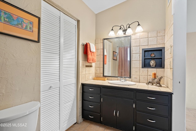 bathroom featuring vanity, toilet, tile patterned floors, and tile walls