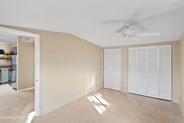 unfurnished bedroom featuring multiple closets, vaulted ceiling, stainless steel fridge, ceiling fan, and light tile patterned floors