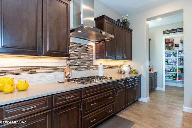 kitchen with light hardwood / wood-style flooring, wall chimney exhaust hood, decorative backsplash, dark brown cabinets, and stainless steel gas cooktop