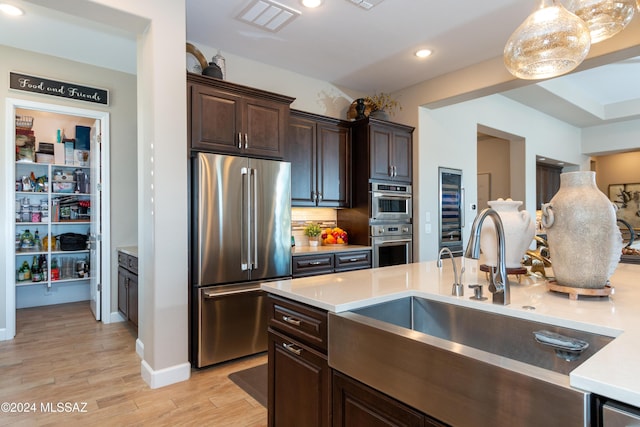 kitchen featuring pendant lighting, sink, light hardwood / wood-style flooring, dark brown cabinetry, and stainless steel appliances