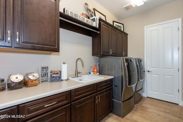 clothes washing area with cabinets, light wood-type flooring, washing machine and dryer, and sink