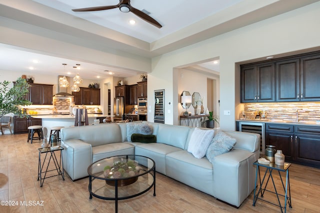 living room with wine cooler, ceiling fan, sink, and light hardwood / wood-style floors