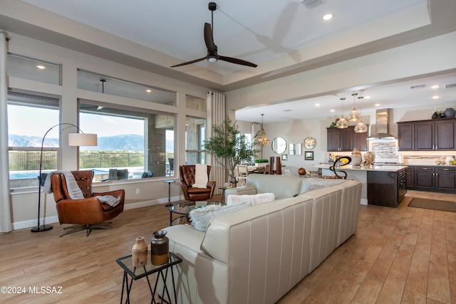 living room featuring a mountain view, light wood-type flooring, a raised ceiling, and ceiling fan