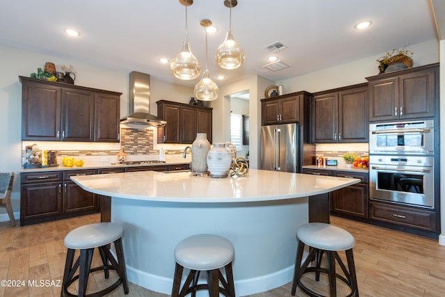 kitchen with a breakfast bar, a center island, wall chimney exhaust hood, decorative light fixtures, and stainless steel appliances