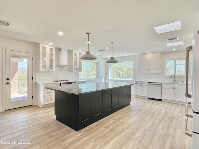 kitchen featuring light wood-style flooring, visible vents, wall chimney range hood, and dishwashing machine