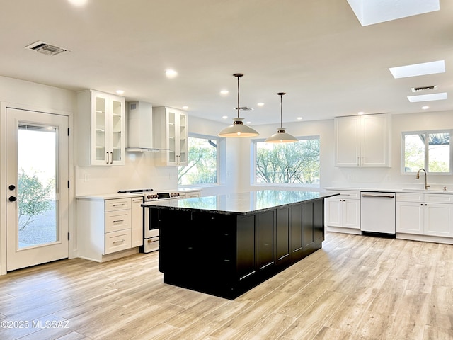 kitchen featuring dishwashing machine, stove, light wood-type flooring, wall chimney range hood, and a sink