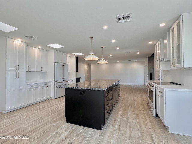 kitchen featuring white electric stove, a kitchen island, visible vents, high end fridge, and wall chimney range hood